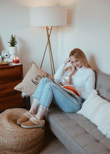 Amanda Weldon reading book on couch with sweater and Cougar-Pronya-Shearling-Mule-Tan