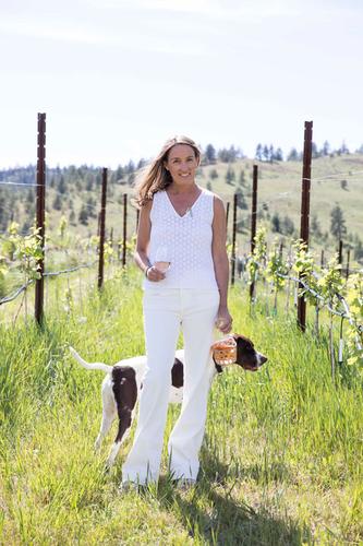 Sarah Bancroft standing in Birch Block Vineyard next to dog in all white and holding glass of wine